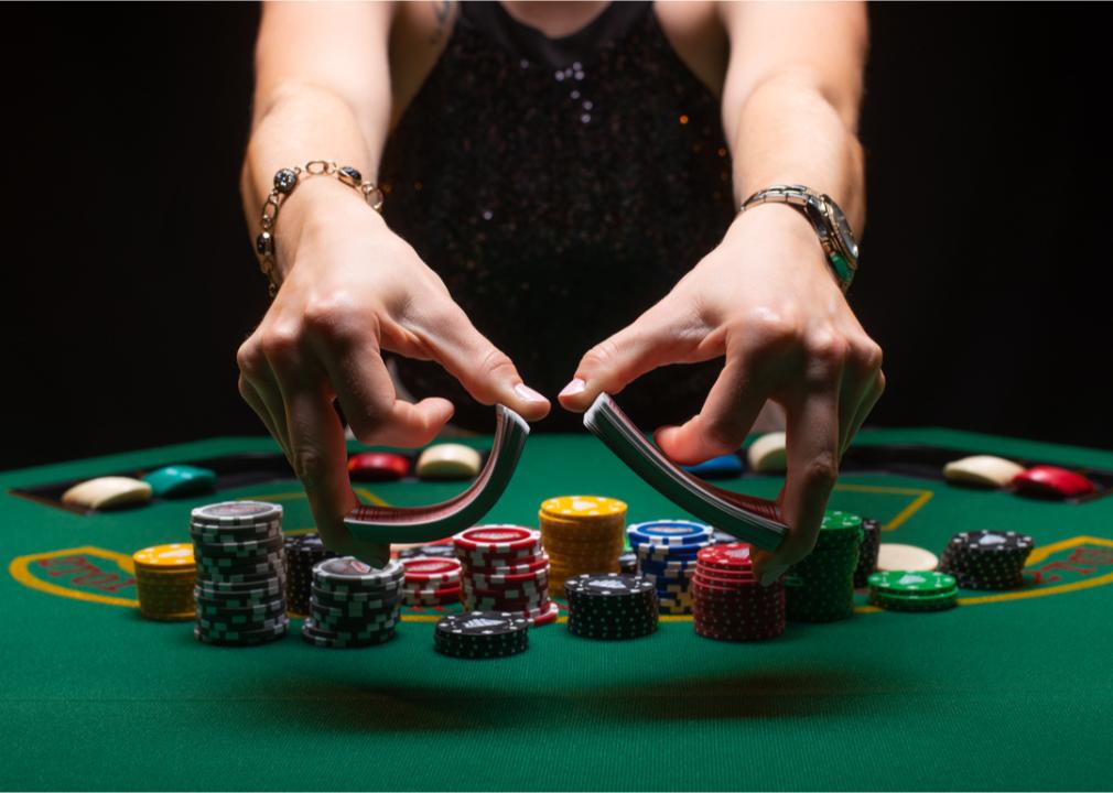 Croupier shuffles poker cards on table with chips.