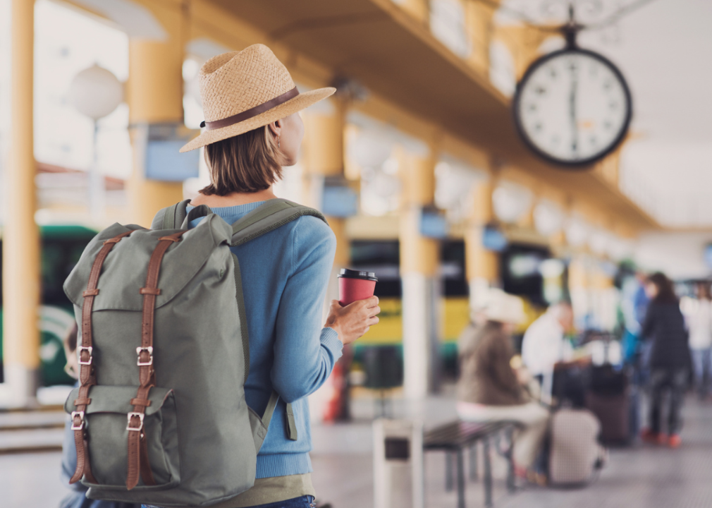 Woman with backpack and coffee at train station in morning