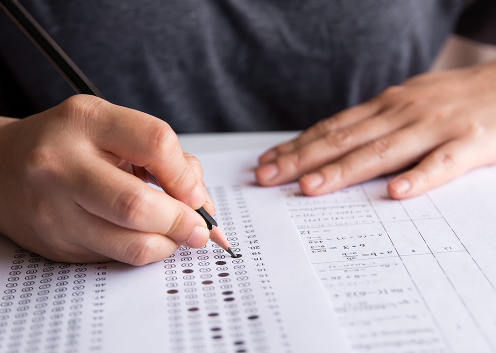 Hand with pencil filling out standardized test form.