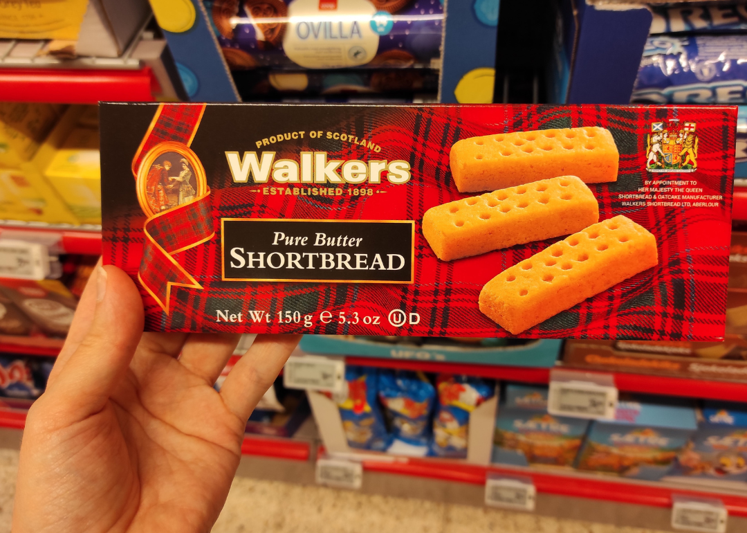 Hand holding package of Walkers Shortbread cookies in supermarket.