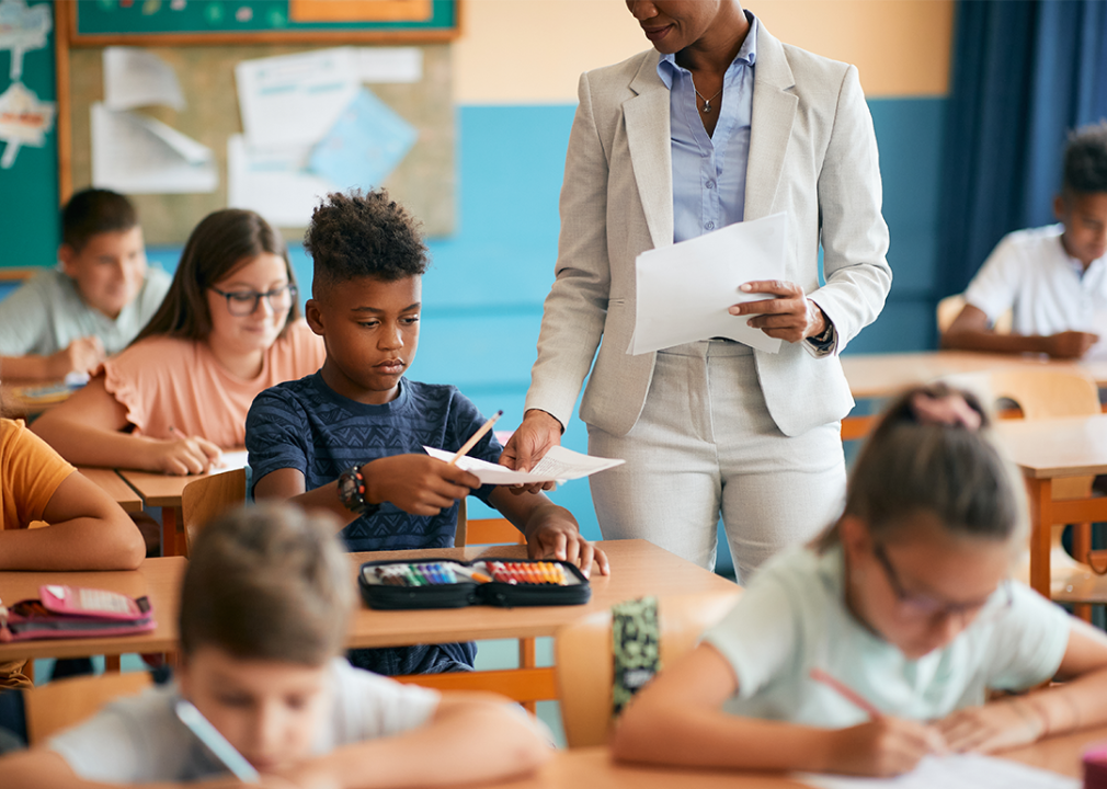 Teacher handing paper to Black student in classroom.