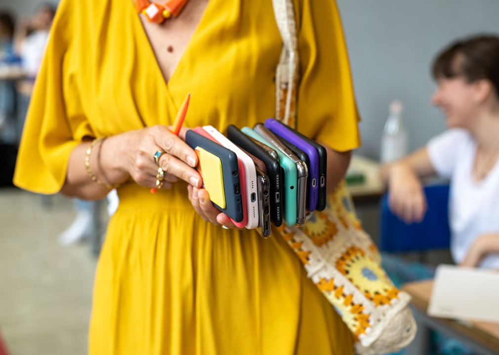 Cropped view of teacher collecting phones in classroom.