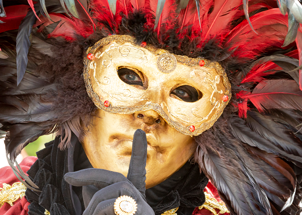 Close view of person wearing gold feathered Venetian mask at festival.