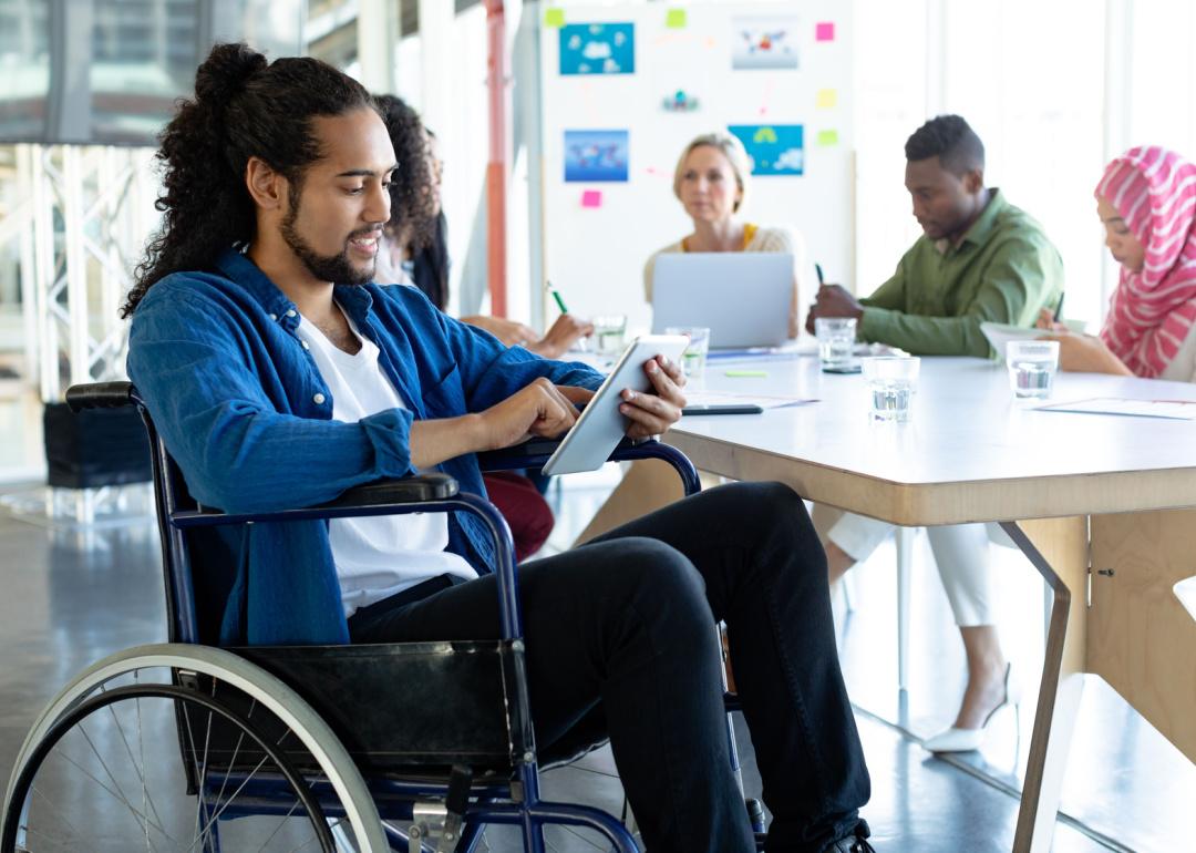 Man in wheelchair using tablet in meeting.