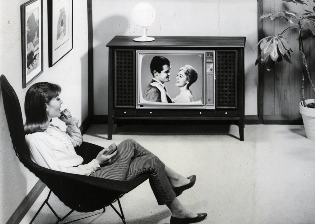 A woman watches a TV program that features a couple in a romantic mood.