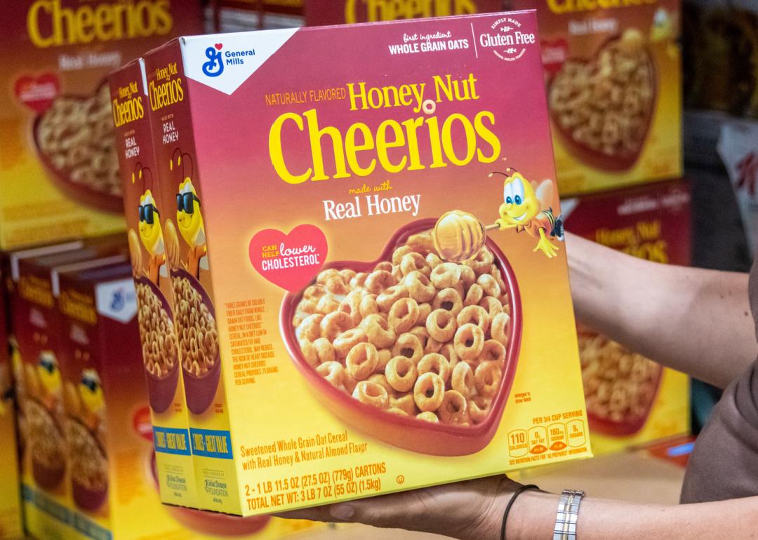 Hand holding large package of Honey Nut Cheerios in supermarket.