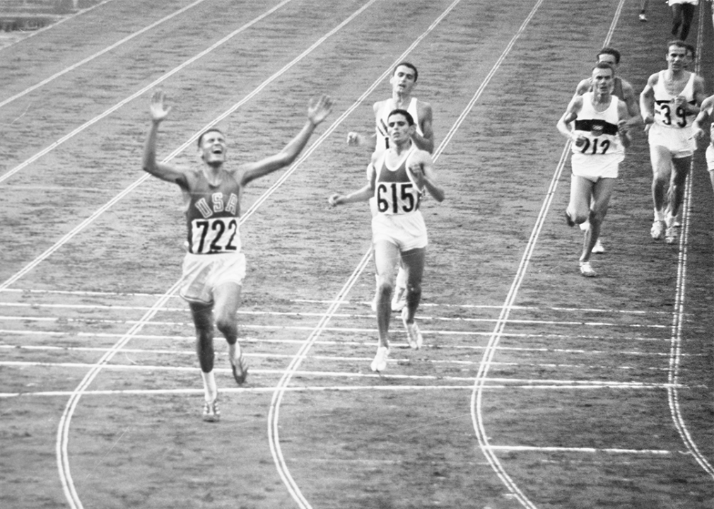Billy Mills raising arms after crossing finish line in 10,000 meter race.