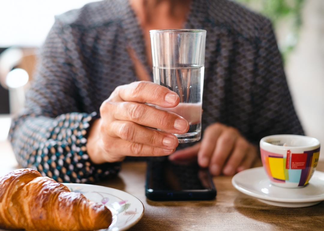 Woman holding a glass of water with coffee and croissant.