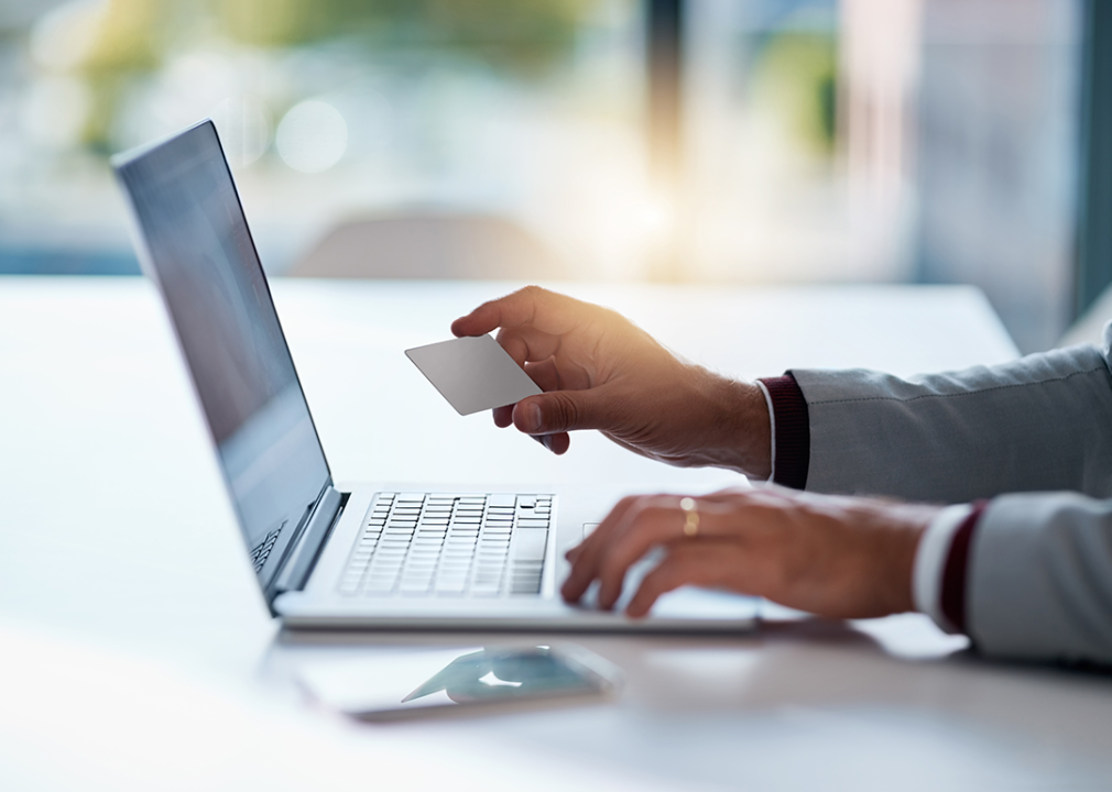 Person holding a credit card in front of a laptop.