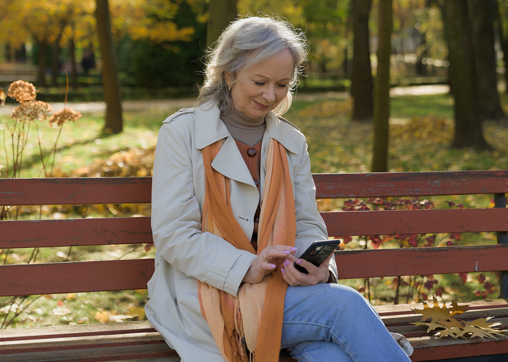 Older woman sitting on park bench looking at phone.
