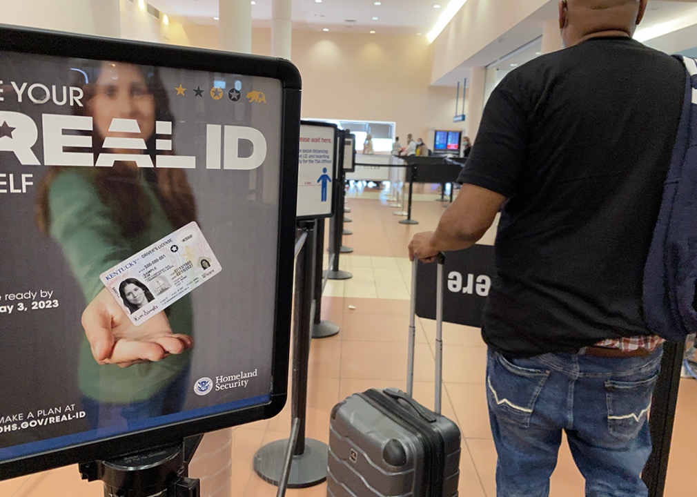 Passenger walking by REAL ID sign at TSA security area in airport.