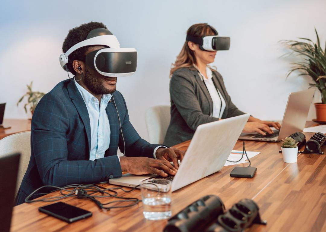 Two office workers with virtual reality headsets working at the table