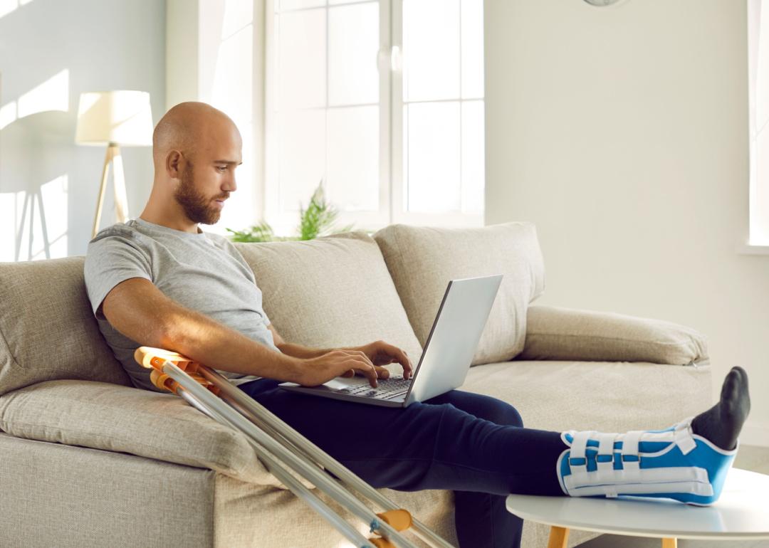 Person on sofa with injured leg looking at laptop computer.
