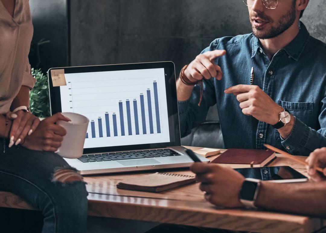 Business team discusses chart on laptop.