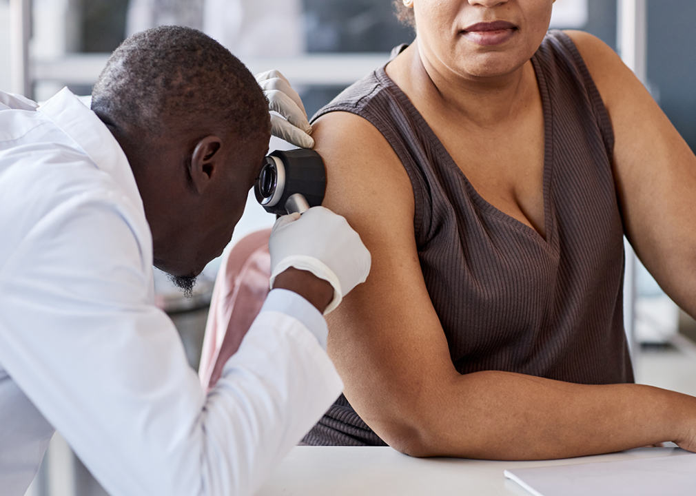Dermatologists examining skin of patient with dermascope.