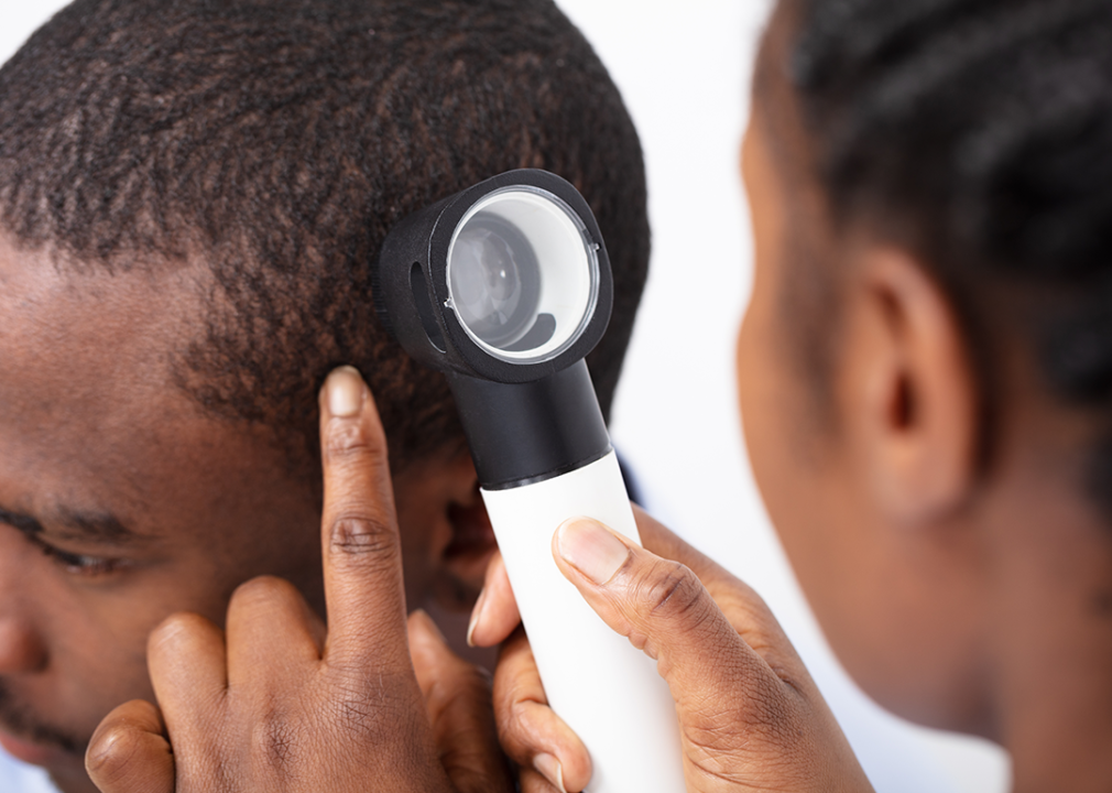 Doctor with dermatoscope checking skin on head.