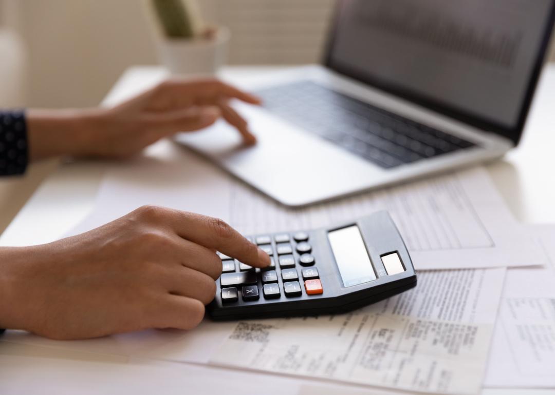 Person with calculator entering information into laptop.