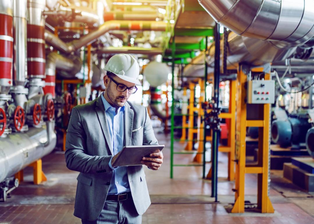 Man in suit and hard hat checks tablet in power plant.