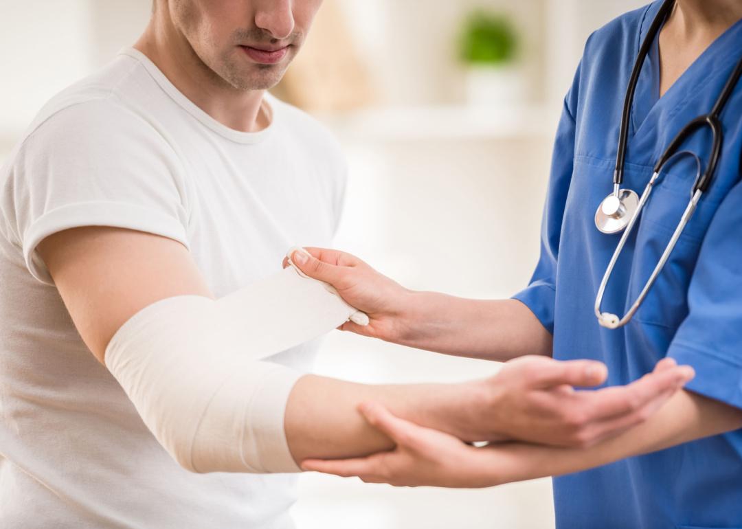 Doctor with stethoscope bandaging hand of patient.