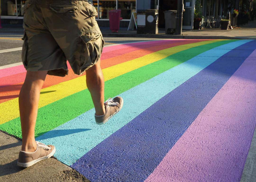 Person walking across a rainbow colored crosswalk