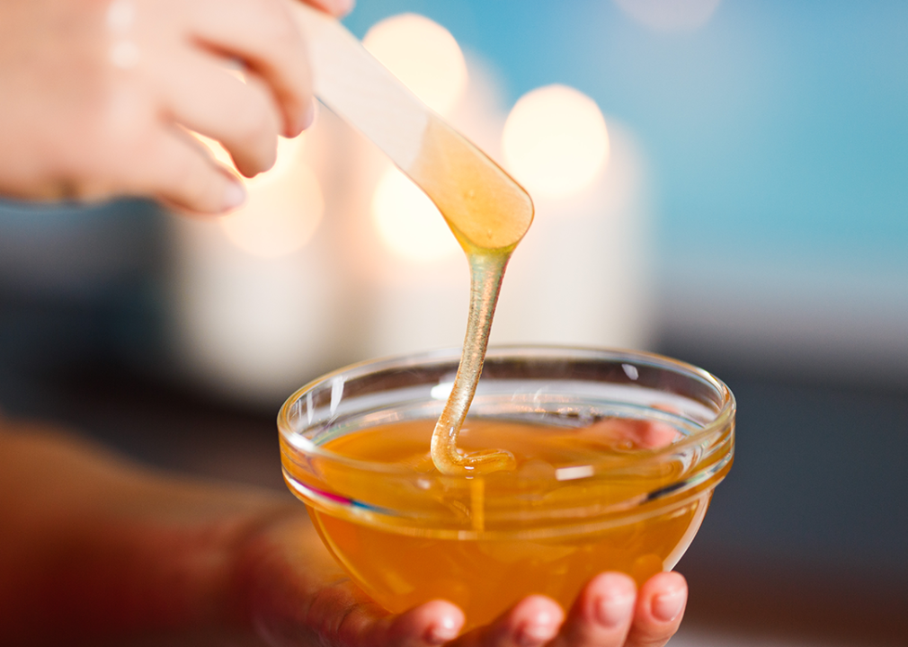 Hand holding bowl of honey with wooden stick.