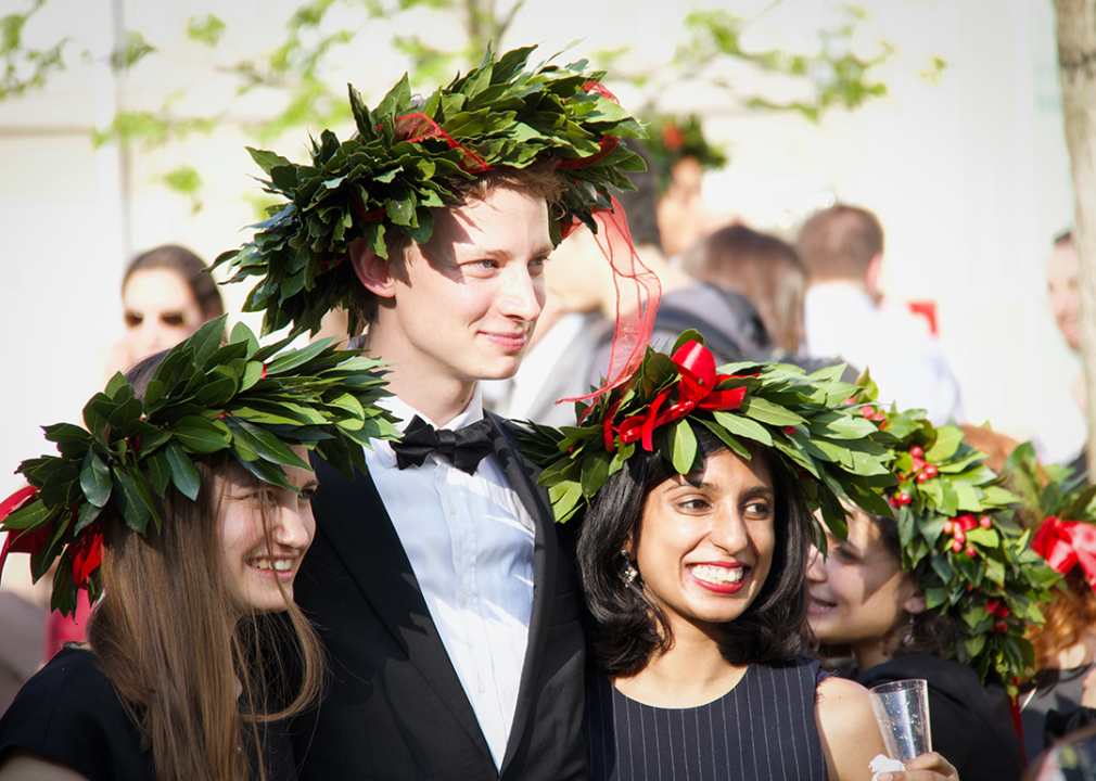 Three graduates wearing laurel wreath celebrate.