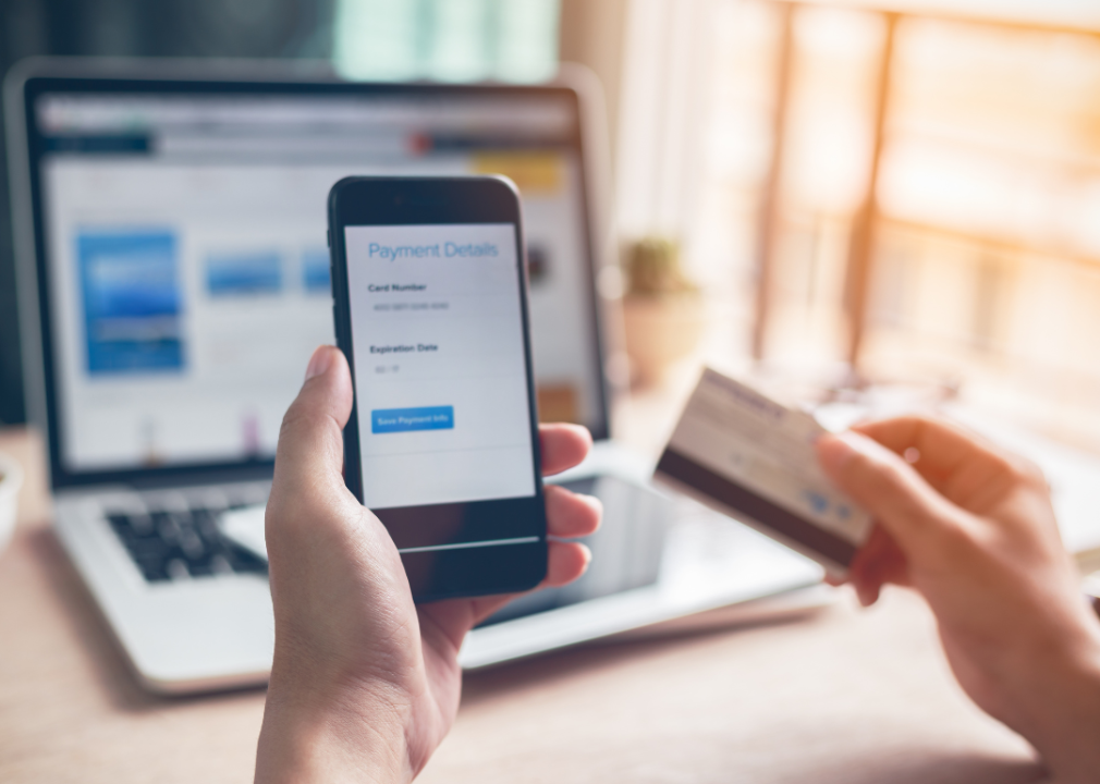 Hands holding smartphone reviewing payment on laptop