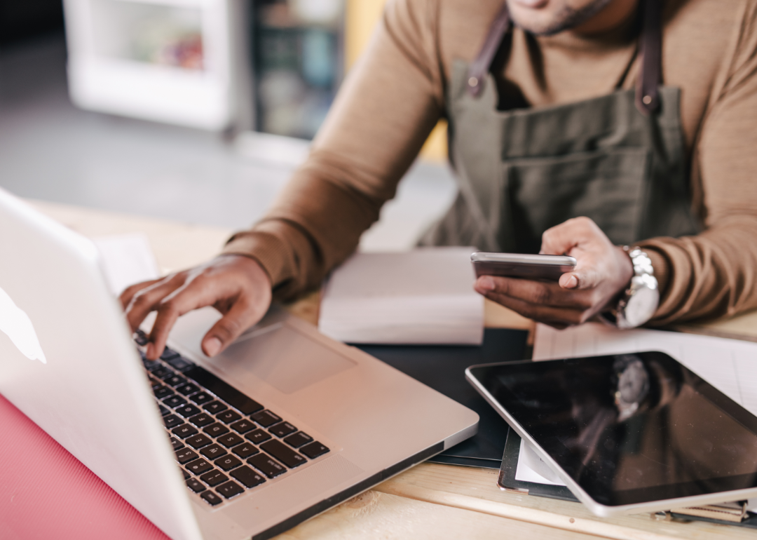 Cropped view of person reviewing information on laptop, phone, and tablet.