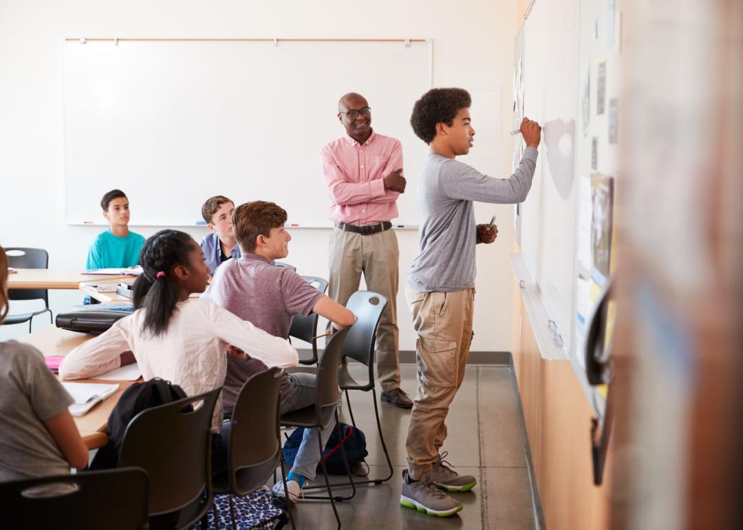 Teacher watches student write on whiteboard in classroom