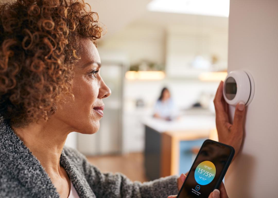 Woman using app to control temperature on thermostat.