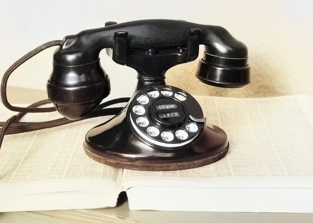 Black rotary dial cradle telephone on telephone number directory book.
