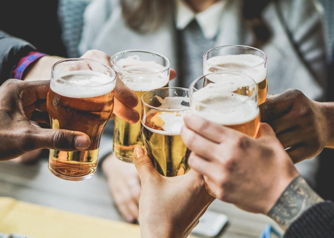 People raise beer glasses together at bar.