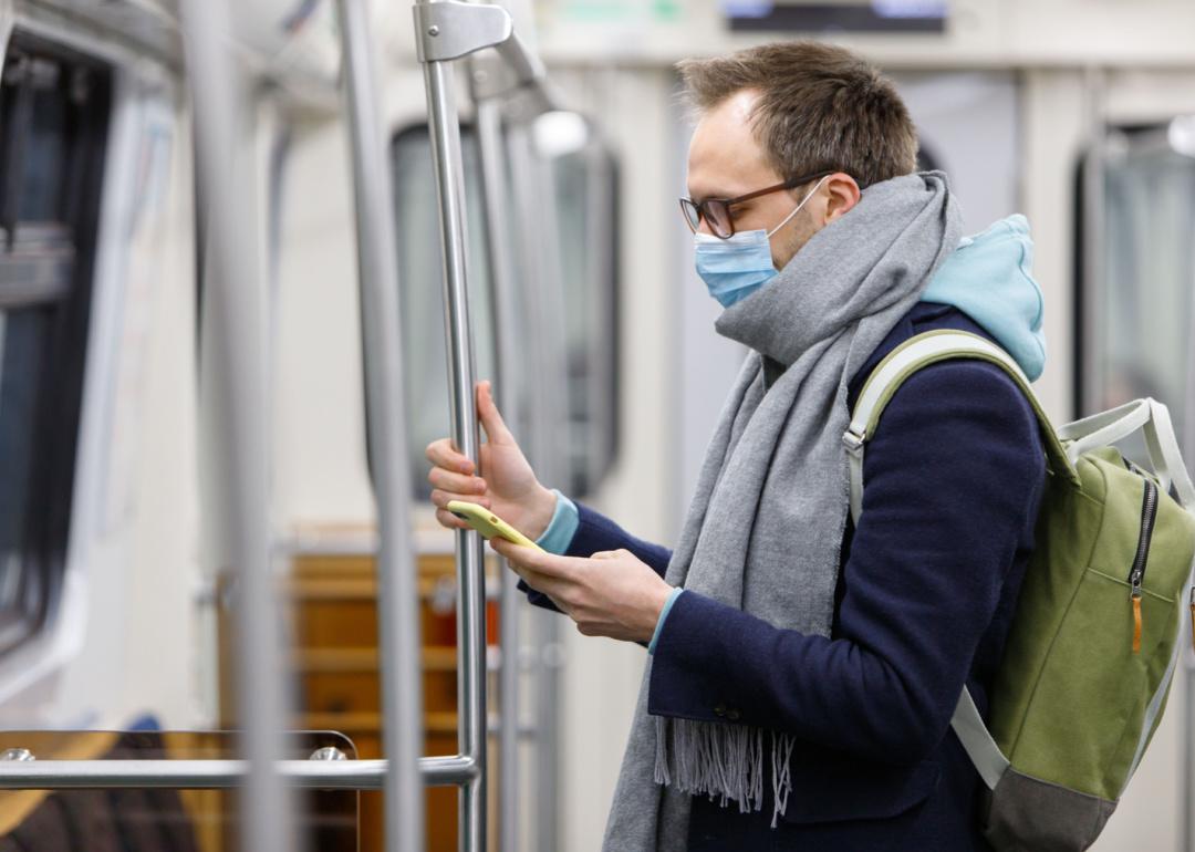 Person riding subway wearing mask, looking at phone.