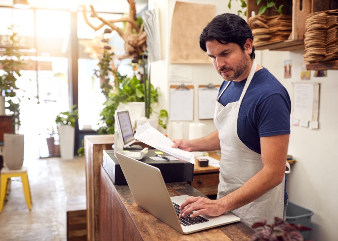 Small business owner at at counter working on laptop.