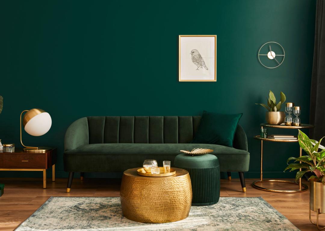 Green living room with velvet sofa and round gold coffee table.
