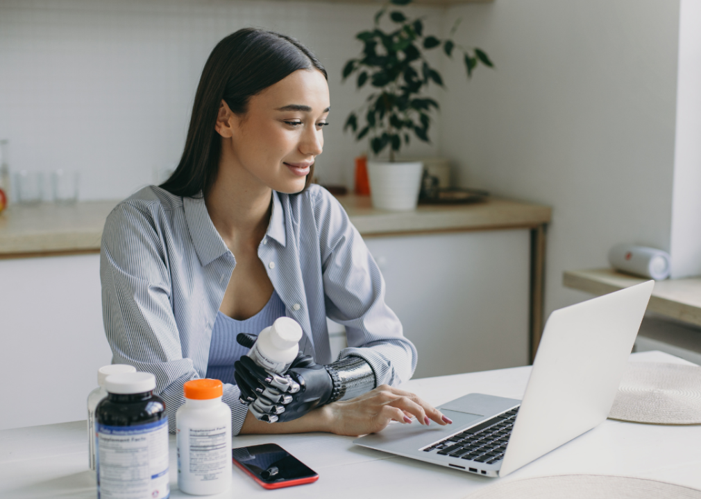 Woman with prosthetic hand holding bottles while on laptop