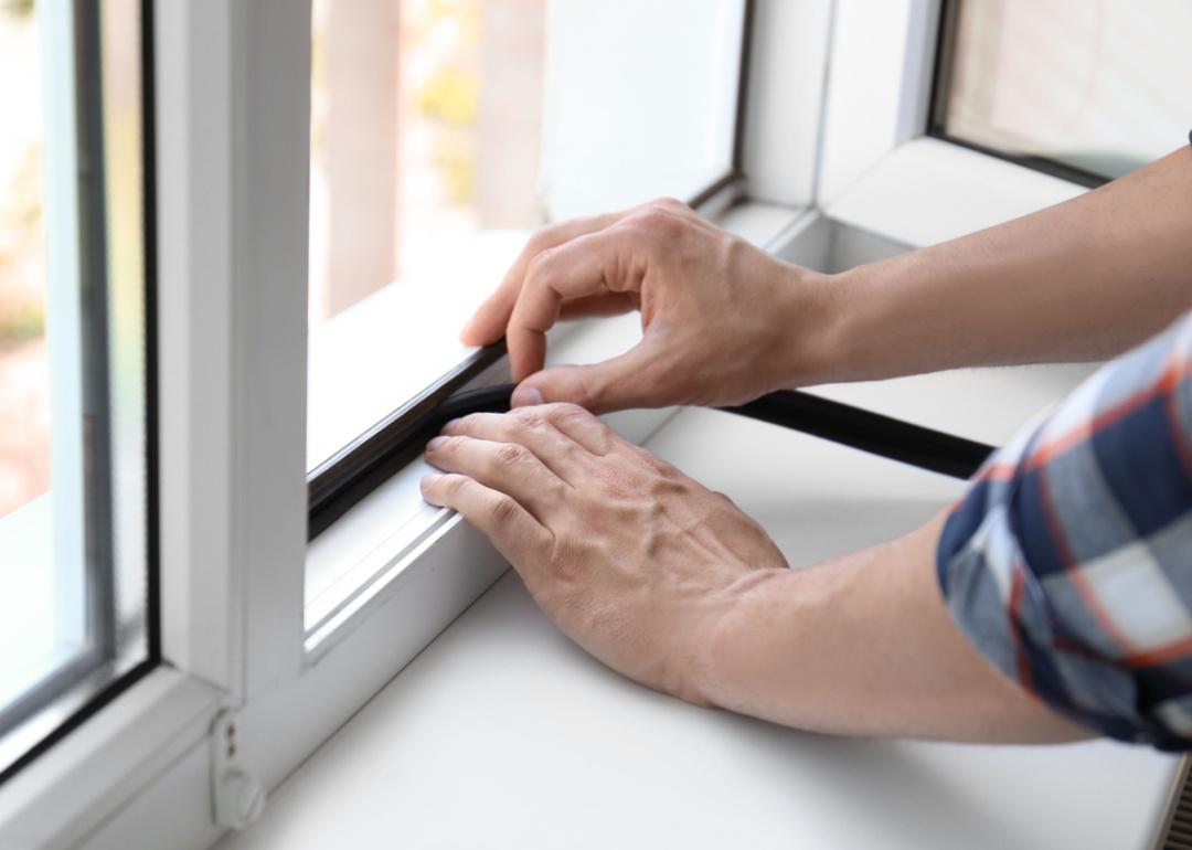 Man putting sealing foam tape on window indoors.