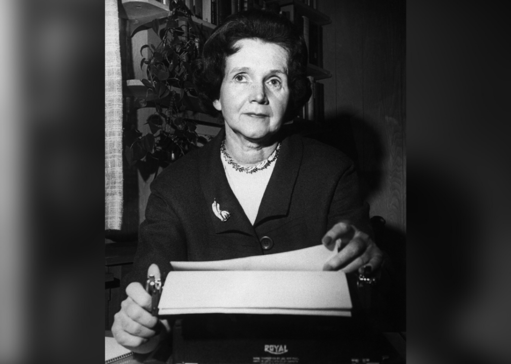 A black and white photo of Rachel Carson looking at the camera while behind a typewriter