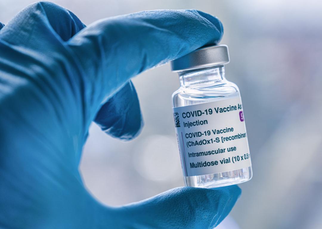 Hand in blue glove holding vial of COVID-19 vaccine.