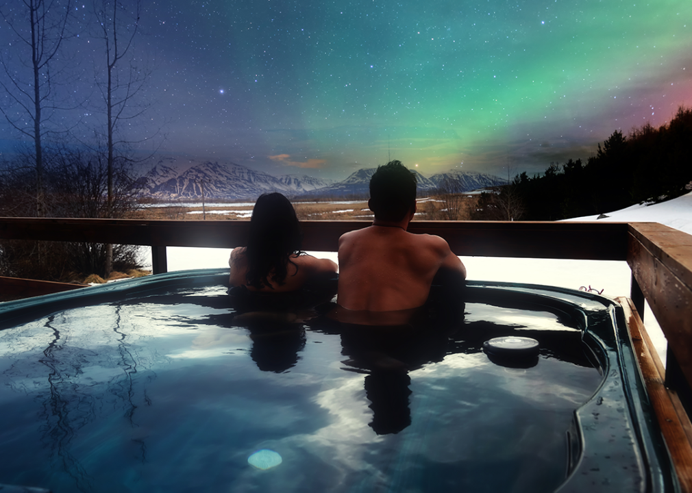 A couple in hot tub at night in Iceland looking at the northern lights.