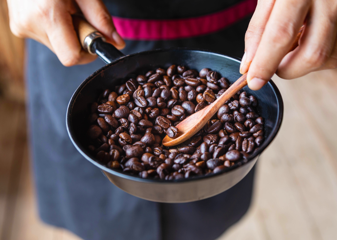 Person checking small pan of coffee beans with wooden spoon.