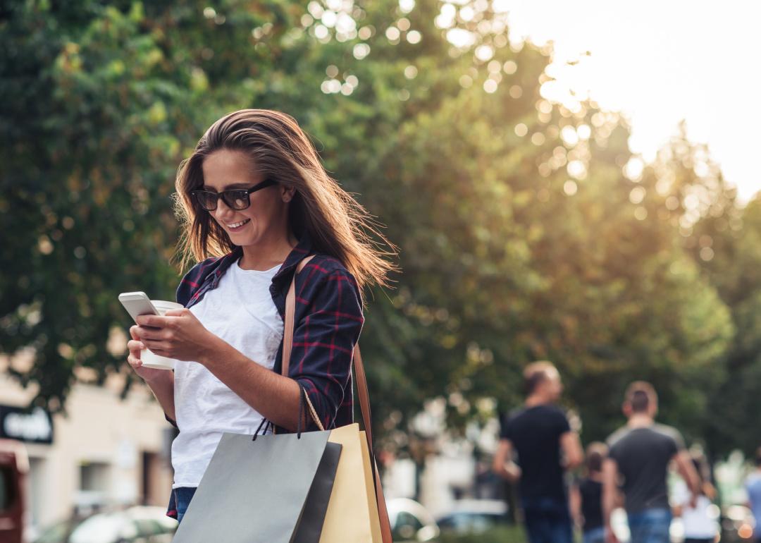 Smiling woman with shopping bags walking looking at phone