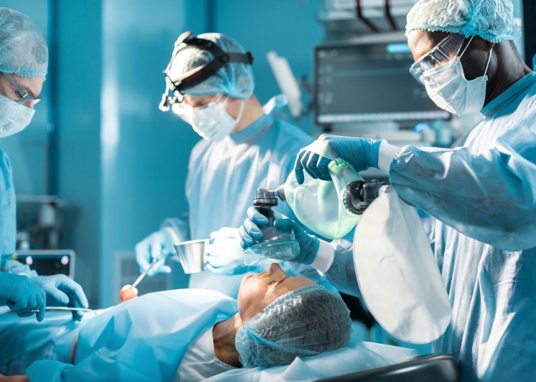 Anesthetist holding oxygen mask above patient.