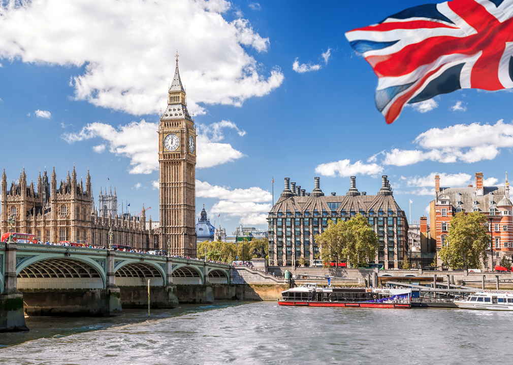 Big Ben with the Thames Bridge and the flag of England against the blue sky.