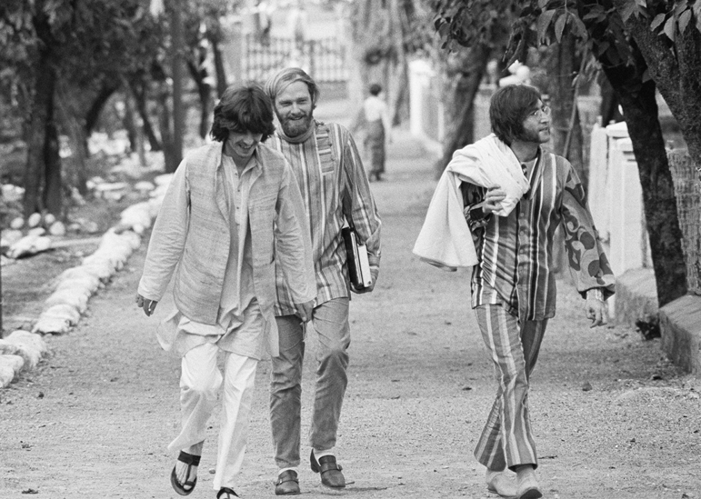 George Harrison, Mike Love, and John Lennon walking and smiling together in India.