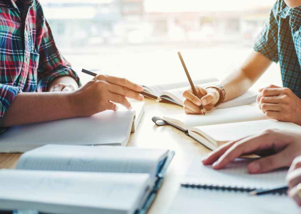 Cropped view of three students with notebooks at table