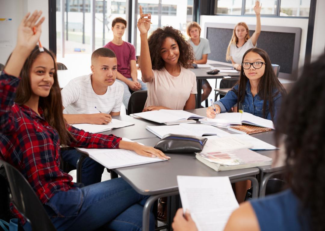 Group of students raise hands in classroom.