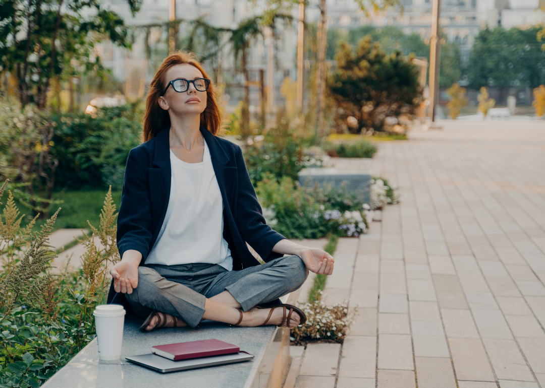 Woman in professional clothing meditating outdoors.