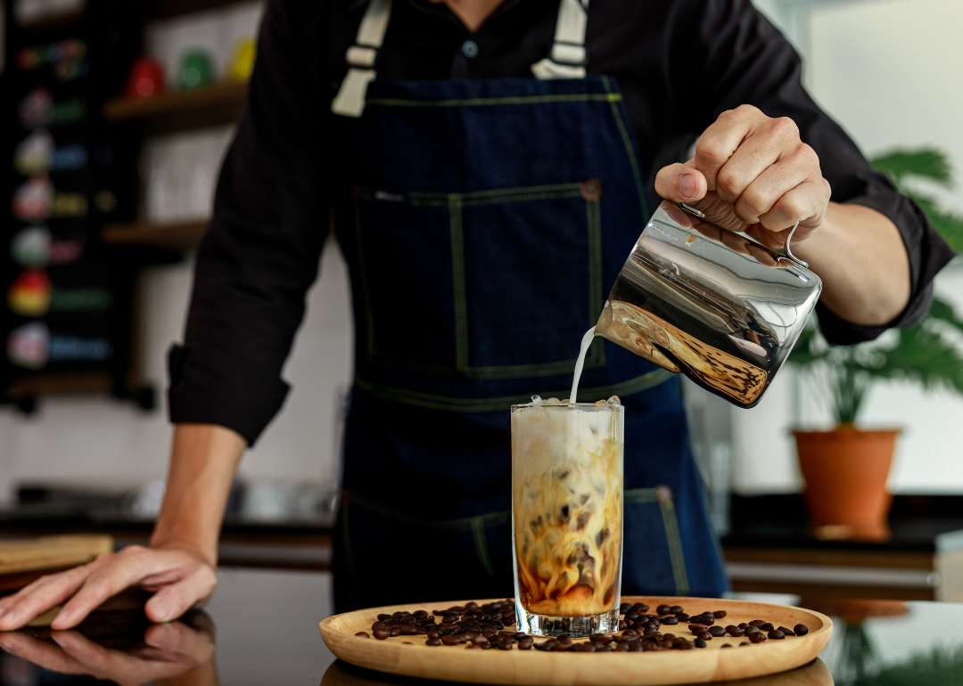 Barista pouring milk in coffee drink.