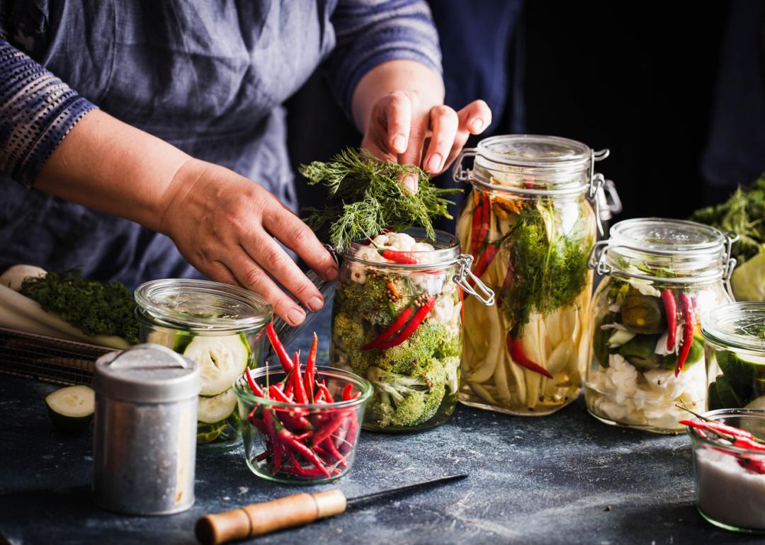 Person preparing pickled vegetables in jars.